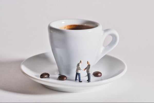 Zwei kleine Figuren schütteln sich die Hände auf der Untertasse vor einem Espresso in der Tasse